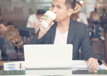 Business man to drinking a tall Starbucks coffee in front of working on a laptop computer.
