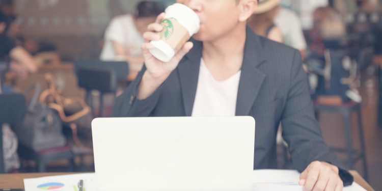Business man to drinking a tall Starbucks coffee in front of working on a laptop computer.