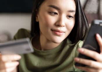 Young asian woman buying from online shop, using mobile phone and credit card, shopping from home.