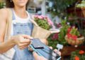 Customer, shopping and credit card for florist shop payment with POS machine or phone for sale of flowers at small business. Hands of woman paying with rfid technology for service at retail store.